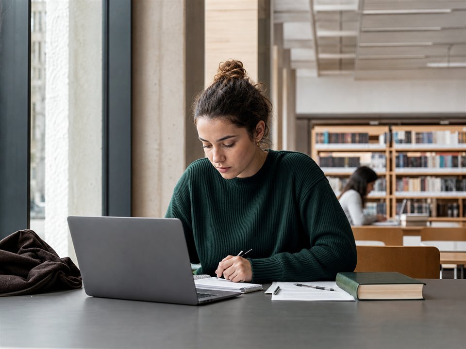 Estudante universitária a trabalhar num portátil numa biblioteca